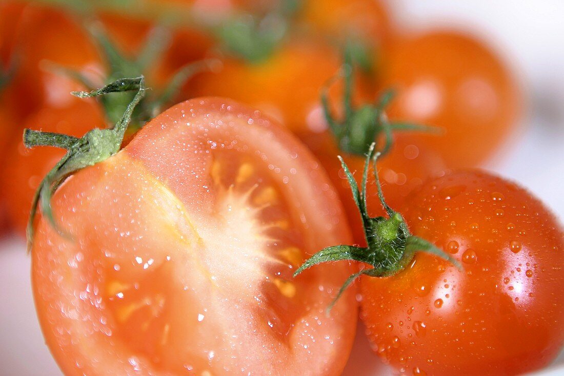 Several ripe, freshly washed tomatoes, some halved