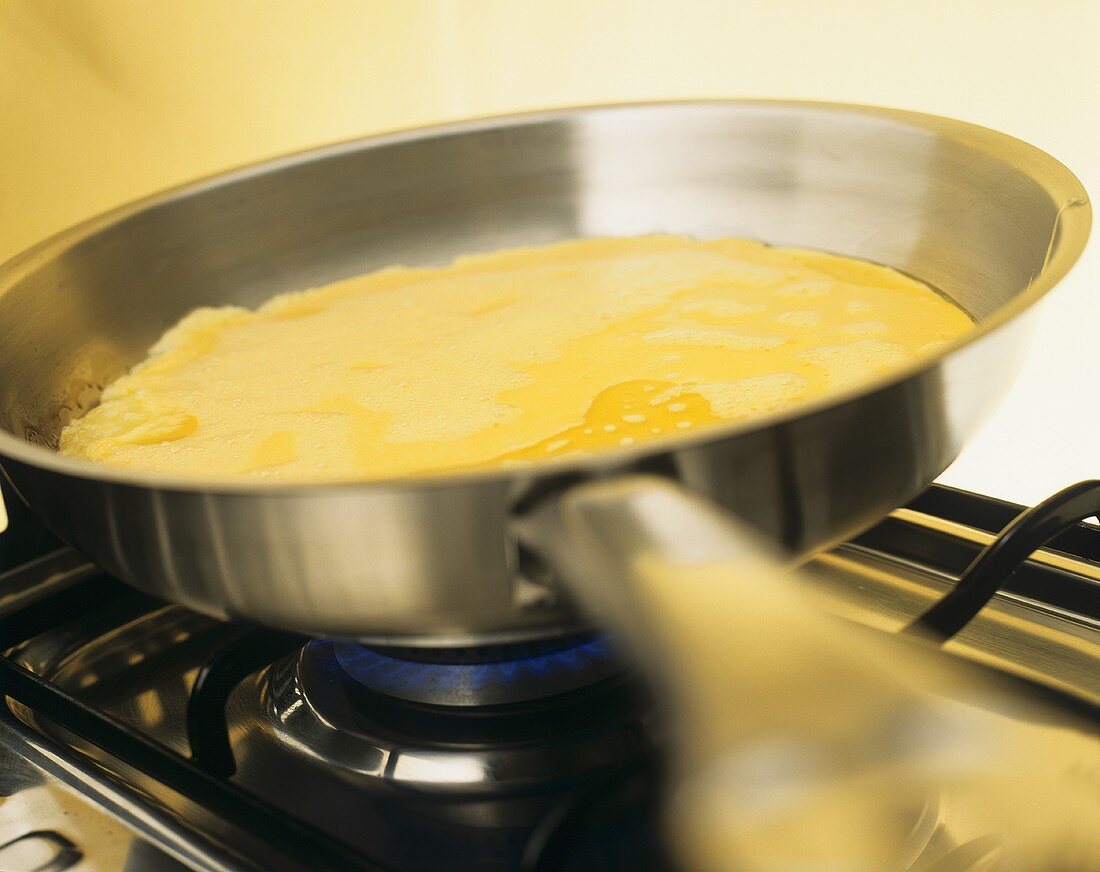 Making omelette in frying pan on gas cooker