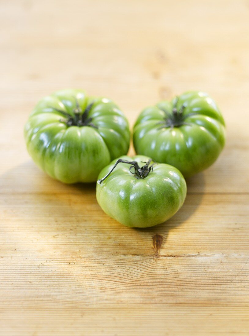 Three green tomatoes on a wooden surface