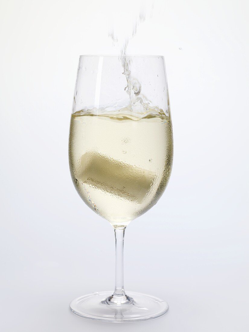 Korken fällt in ein Glas Weißwein