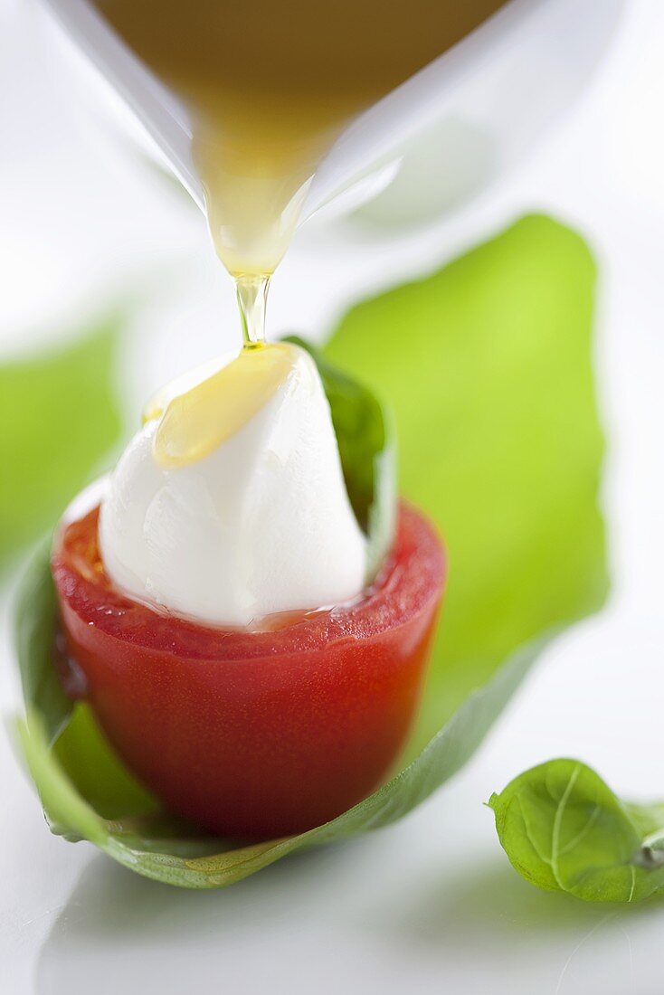 Pouring olive oil on tomato stuffed with mozzarella and basil