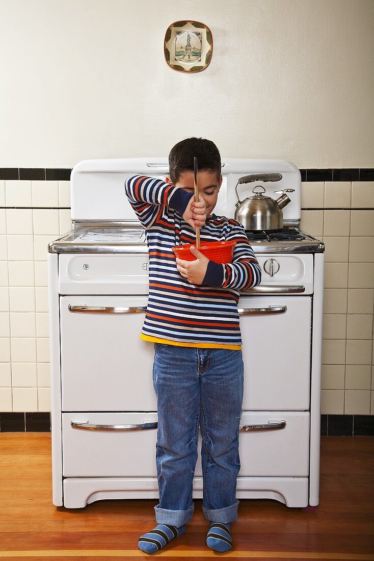 Kleiner Junge mit Rührschüssel vor dem Küchenherd