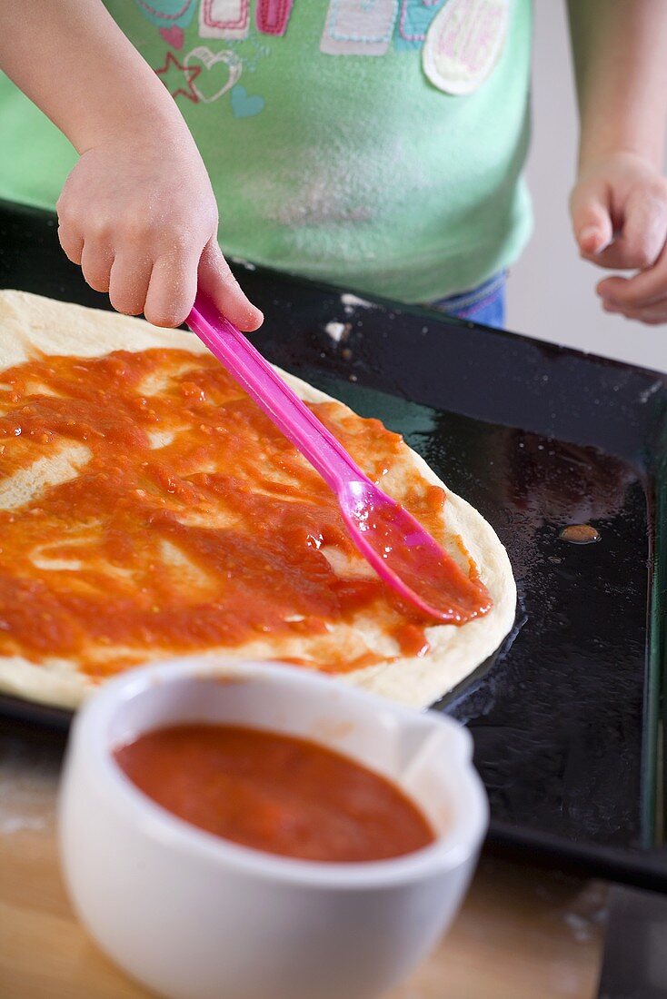 Kleines Kind verteilt Tomatensauce auf Pizzateig