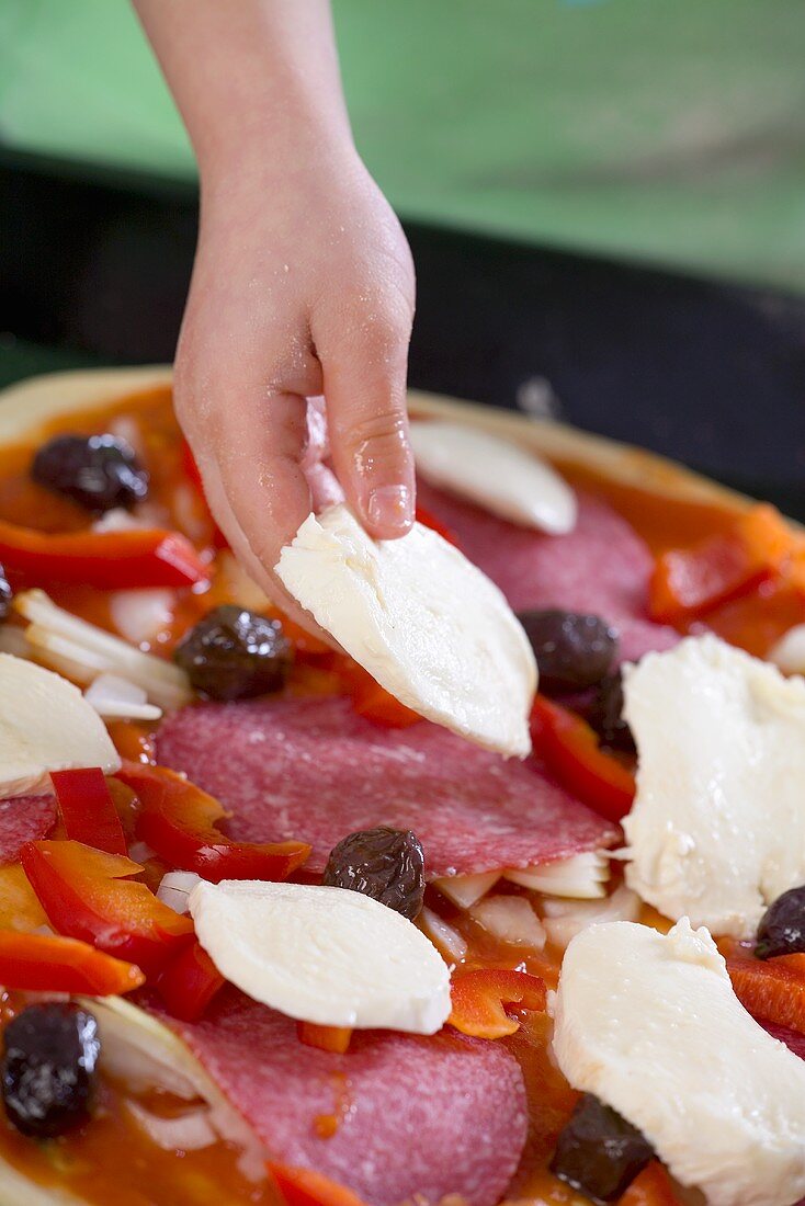 Child's hand putting slices of mozzarella on a pizza