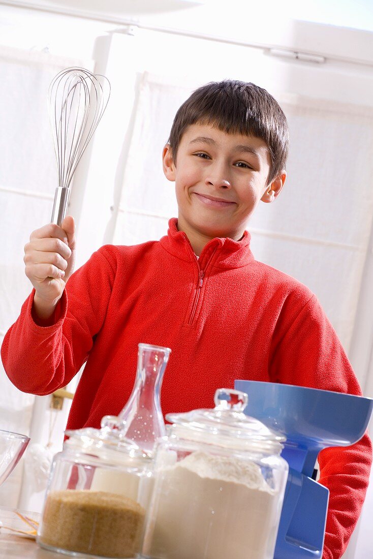 Junge mit Schneebesen in der Hand und Backzutaten