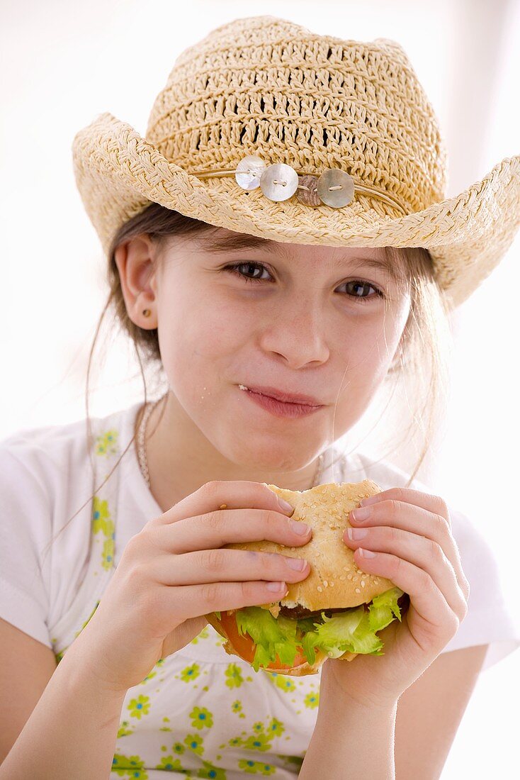 Mädchen mit Hut isst selbstgemachten Hamburger