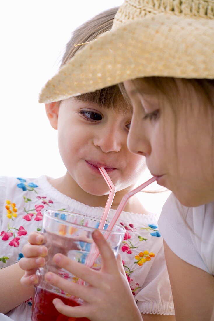 Zwei Mädchen trinken Fruchtsaft mit Strohhalm aus einem Glas