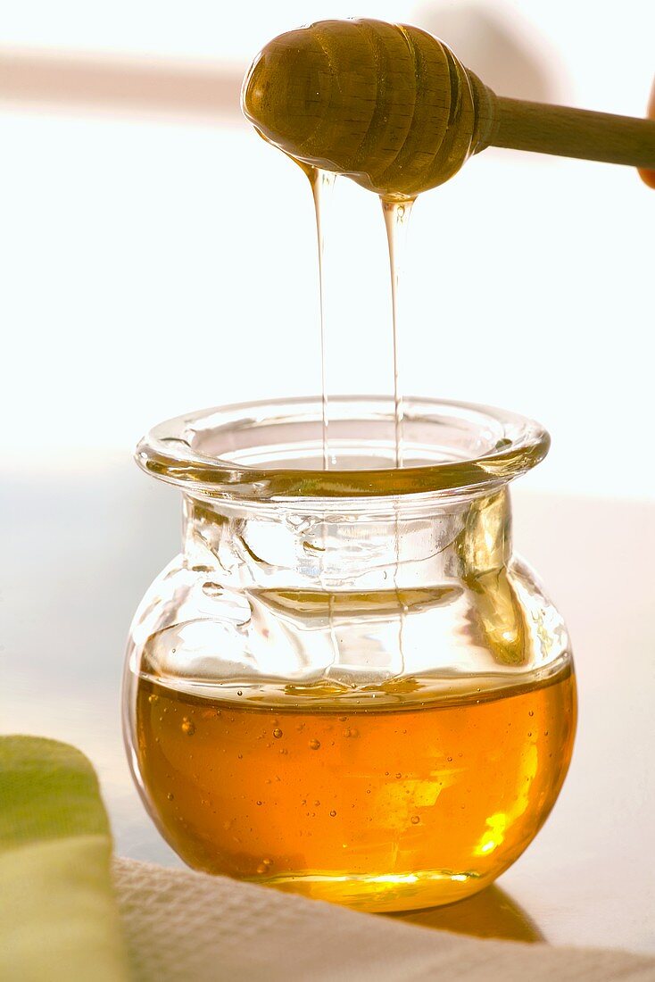 Honey running from honey dipper into jar