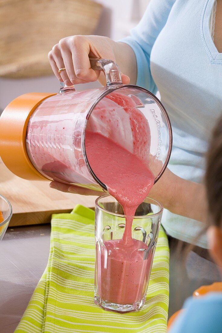 Pouring strawberry milkshake into glass