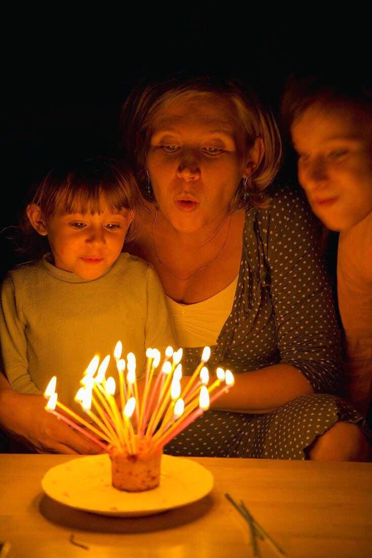 Mutter und Töchter pusten Kerzen auf Geburtstagkuchen aus