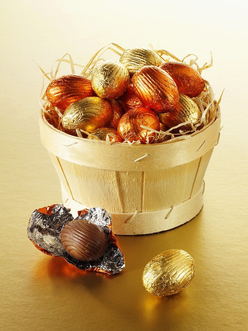 Foil-wrapped chocolate eggs in and beside a woodchip basket