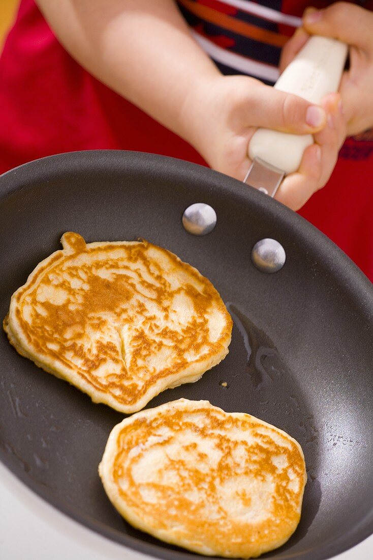 Child's hands holding a frying pan with pancakes