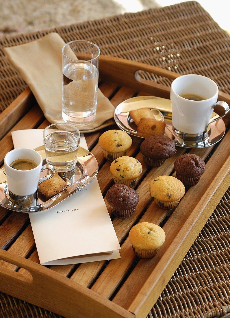 Muffins und Kaffee mit Wassergläsern auf einem Tablett
