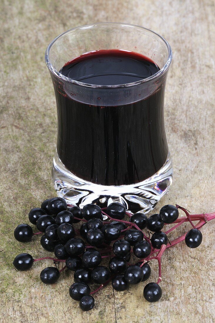 Holunderbeersaft im Glas und frische Holunderbeeren