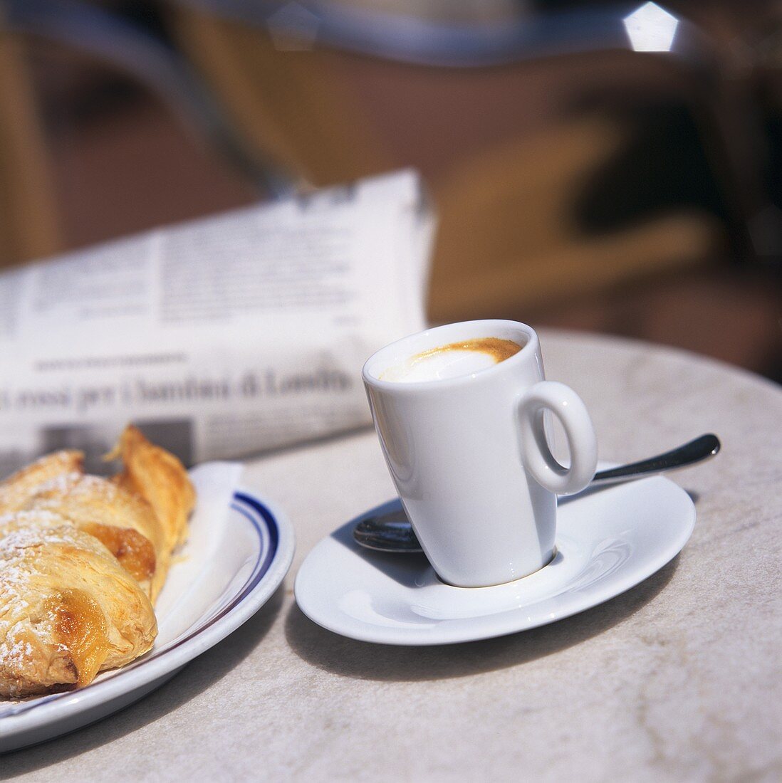 Kaffee Macchiato mit Brioche und Zeitung