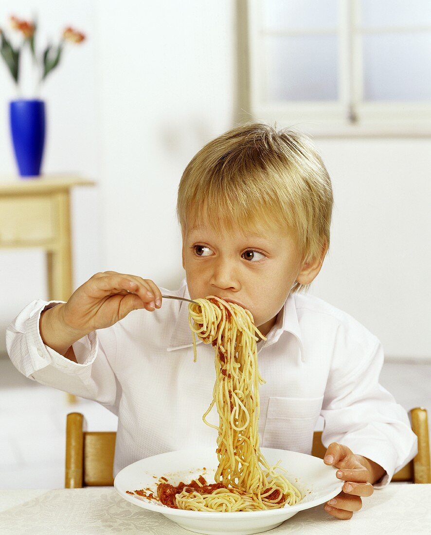 Boy eating spaghetti with tomato sauce