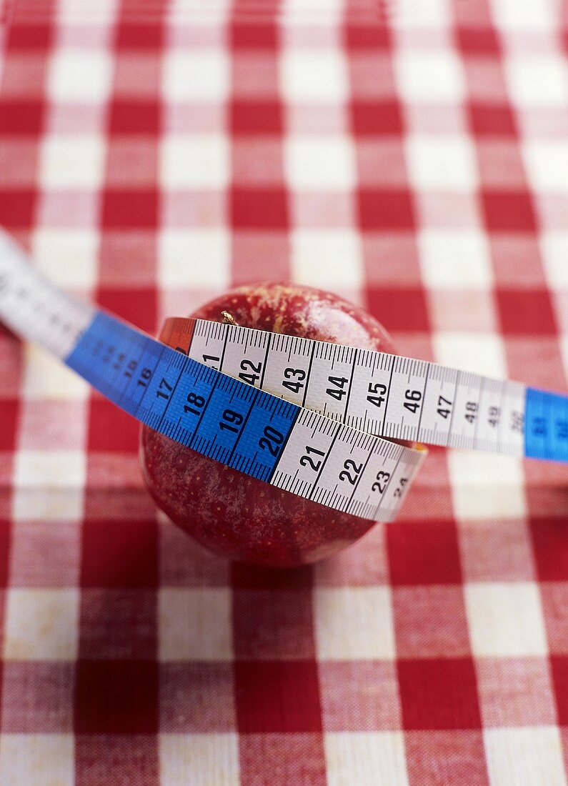 A red apple with a tape measure wrapped around it