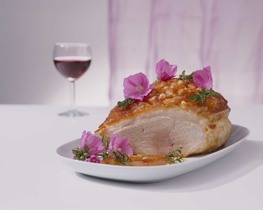 Roast pork with crackling, partly carved, with edible flowers