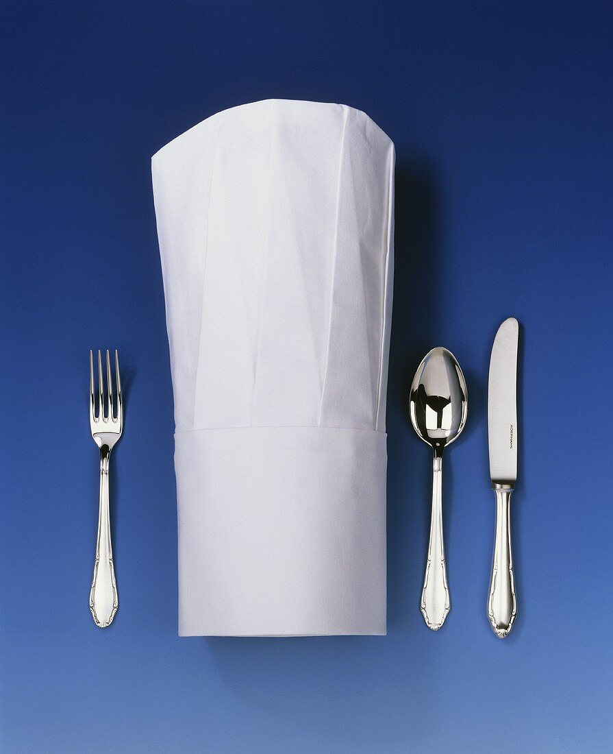 Chef's hat lying between knife, spoon and fork