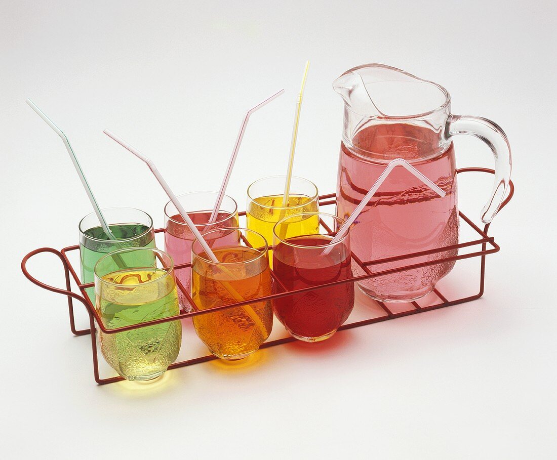Different coloured soft drinks in glasses and glass jug