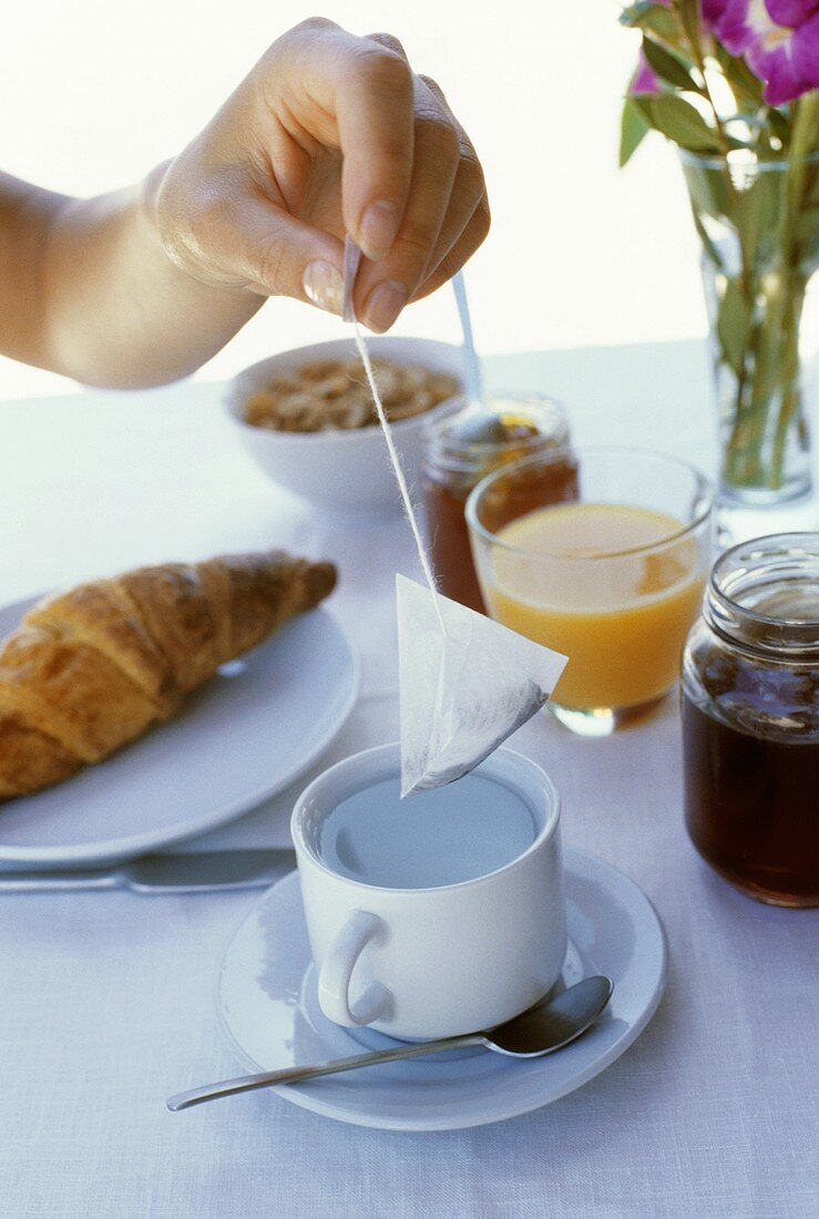 Laid breakfast table: hand holding tea bag over teacup