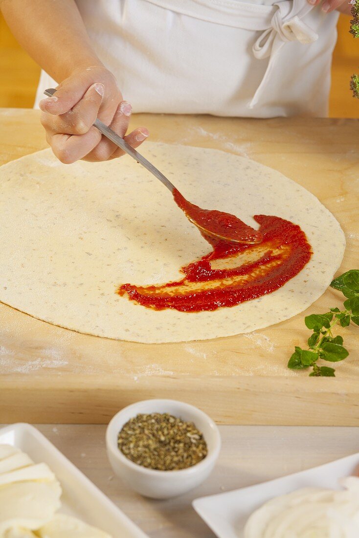 Mädchen bestreicht Pizzateig mit Tomatensauce