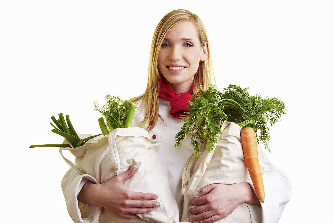 Blonde Köchin hält zwei Jutebeutel mit Gemüse