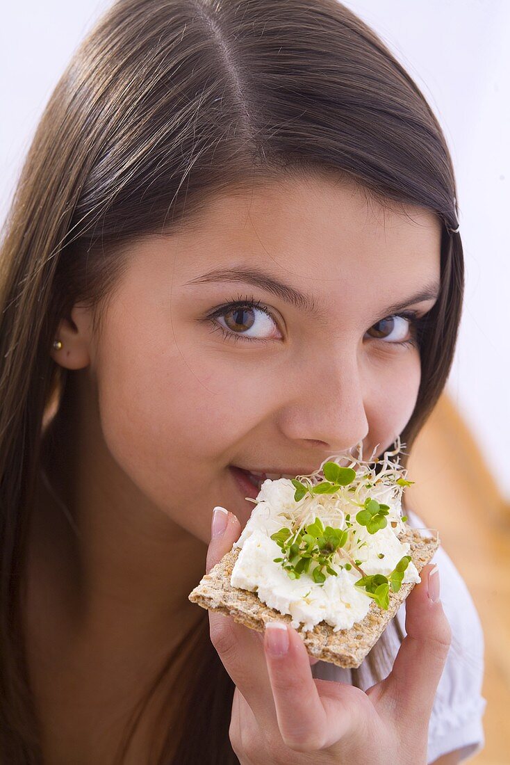 Mädchen isst Knäckebrot mit Hüttenkäse und Kresse