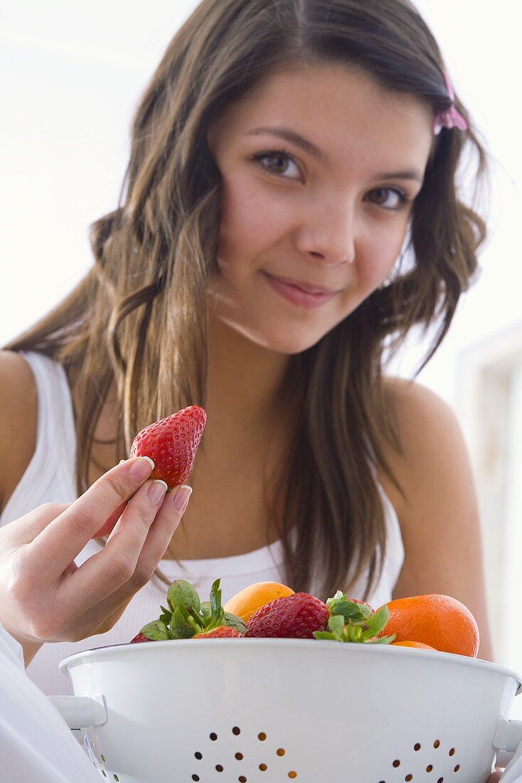 Mädchen hält Erdbeere und Küchensieb mit frischem Obst