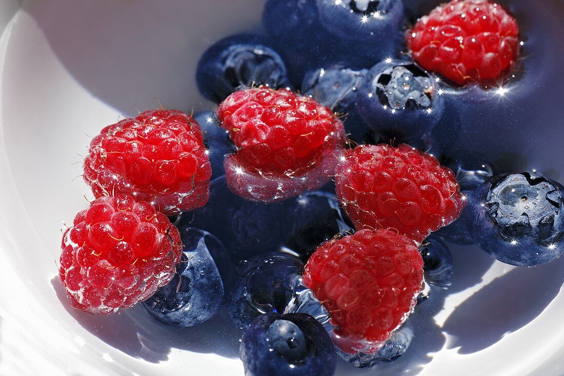 Raspberries and blueberries in a bowl of water