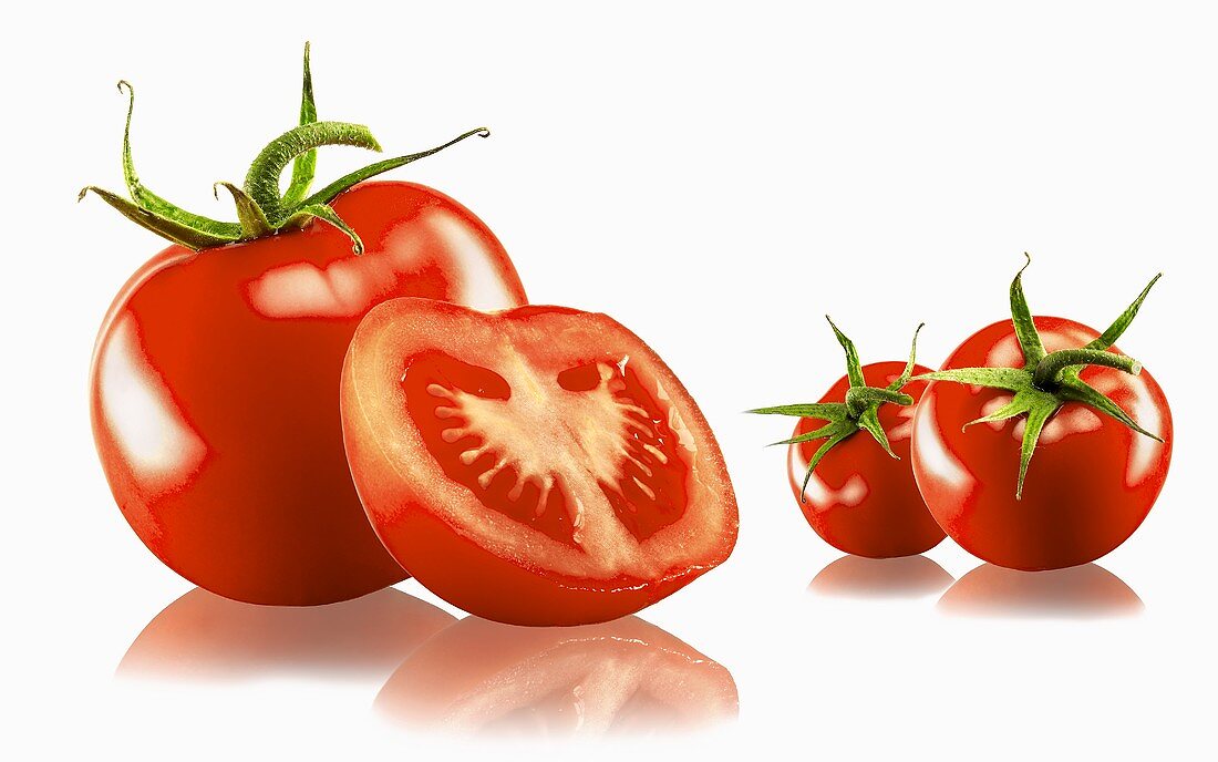 Drei ganze und eine halbierte Tomate auf weißem Grund mit Spiegelung