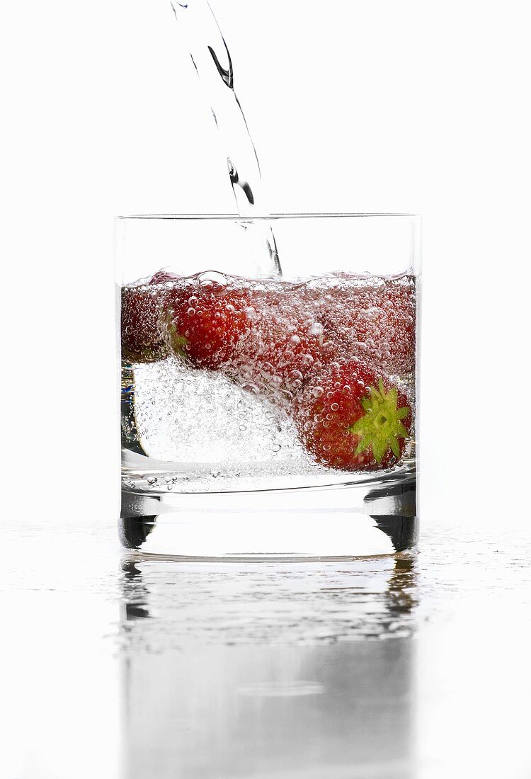 Mineralwasser in Glas mit Erdbeeren gießen