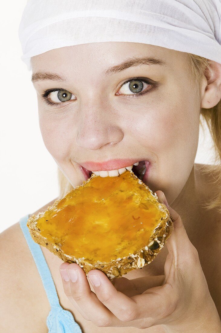 Young woman with headscarf biting into a slice of bread with jam