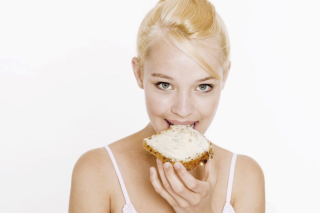 Woman with blond hair biting into a slice of bread and butter