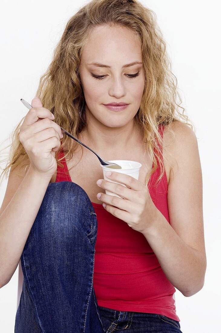 Junge Frau hält einen Becher Joghurt in der Hand