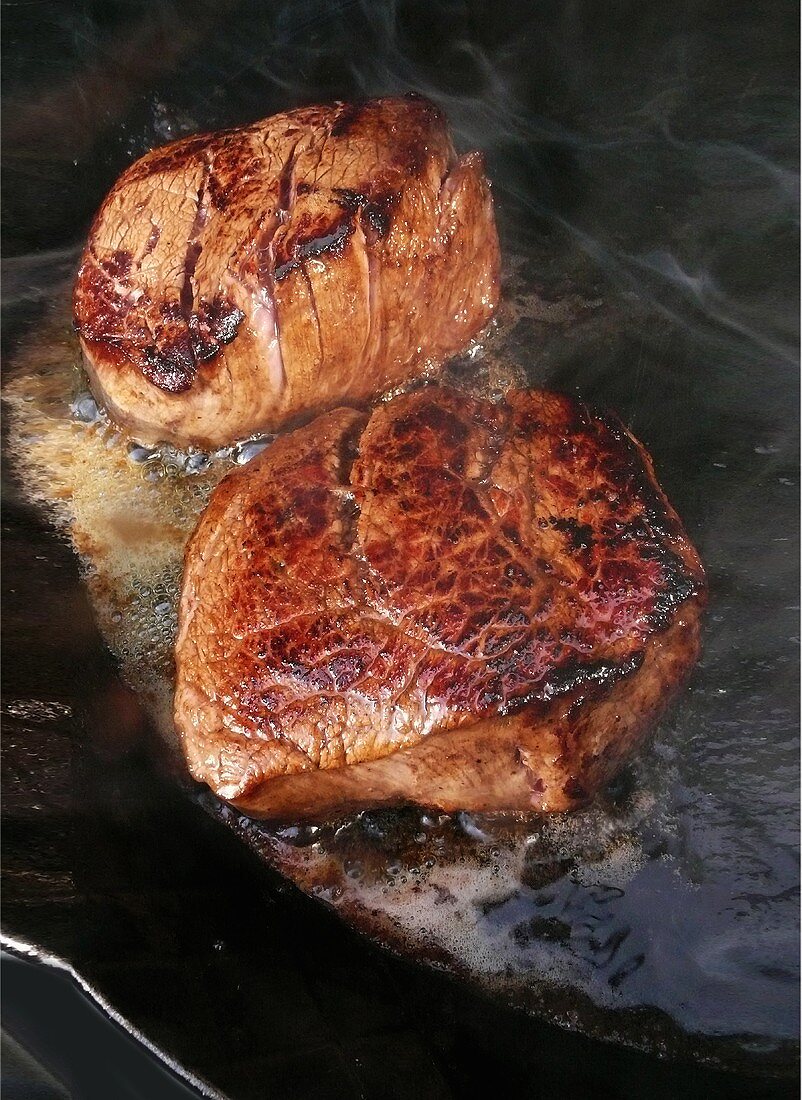 Fillet steaks sizzling in frying pan