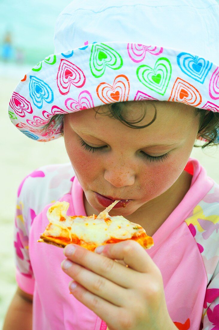 Child eating pizza on the beach