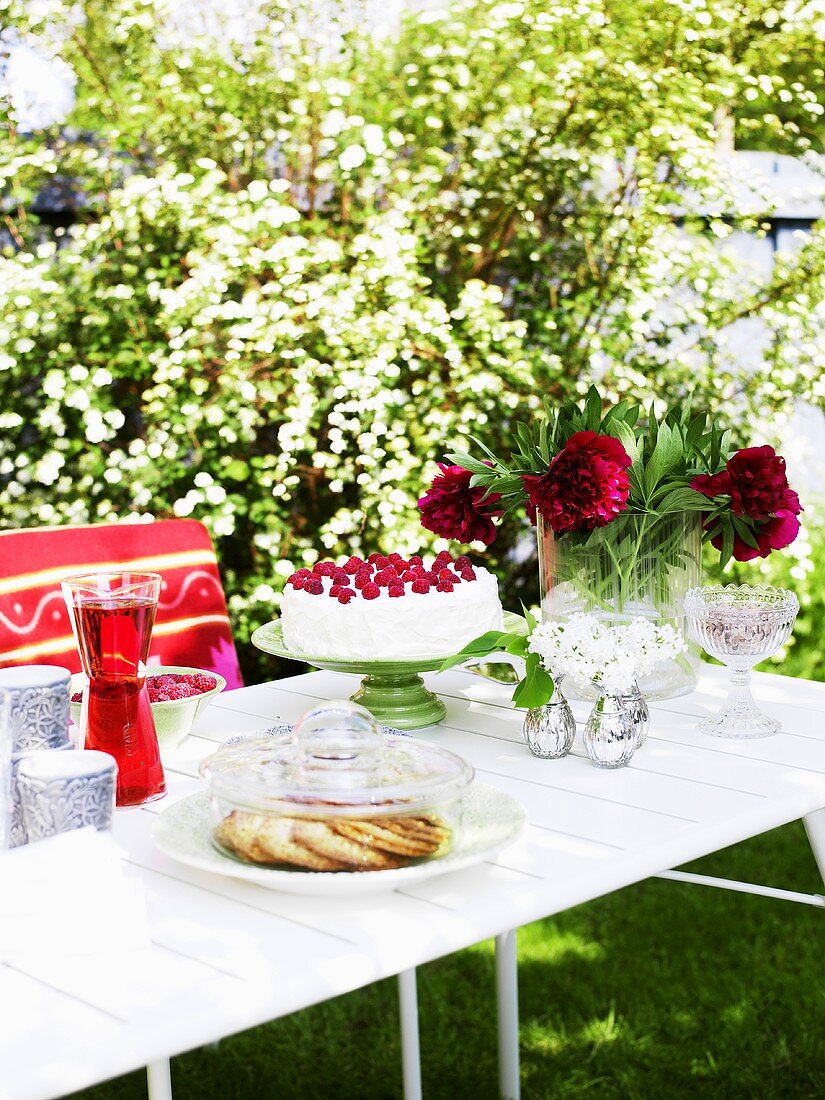 Gedeckter Tisch im Garten mit Kuchen, Gebäck und Saft