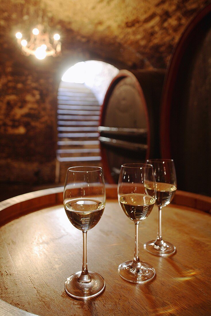 Drei Gläser Weißwein auf Holzfass in einem Weinkeller