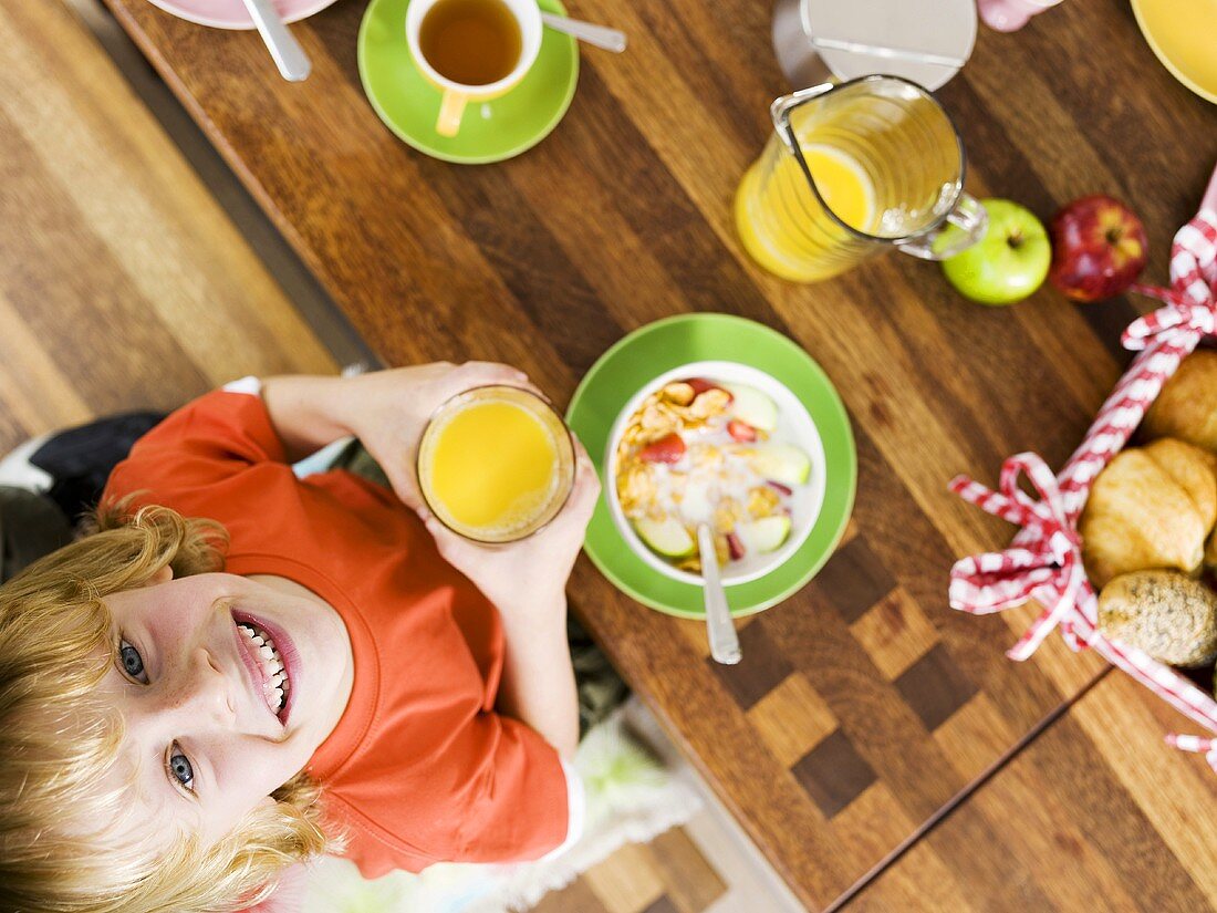 Junge sitzt mit Orangensaft am Frühstückstisch (von oben)
