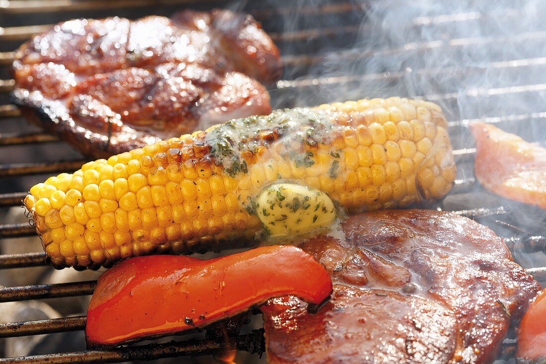 Corn on the cob with herb butter, pork steaks & pepper on barbecue