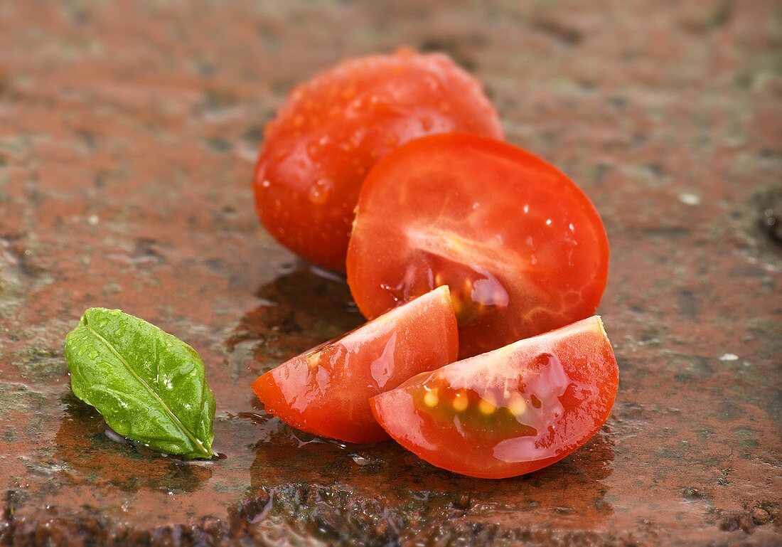 Gewaschene Tomaten und Basilikumblatt auf nassem Stein