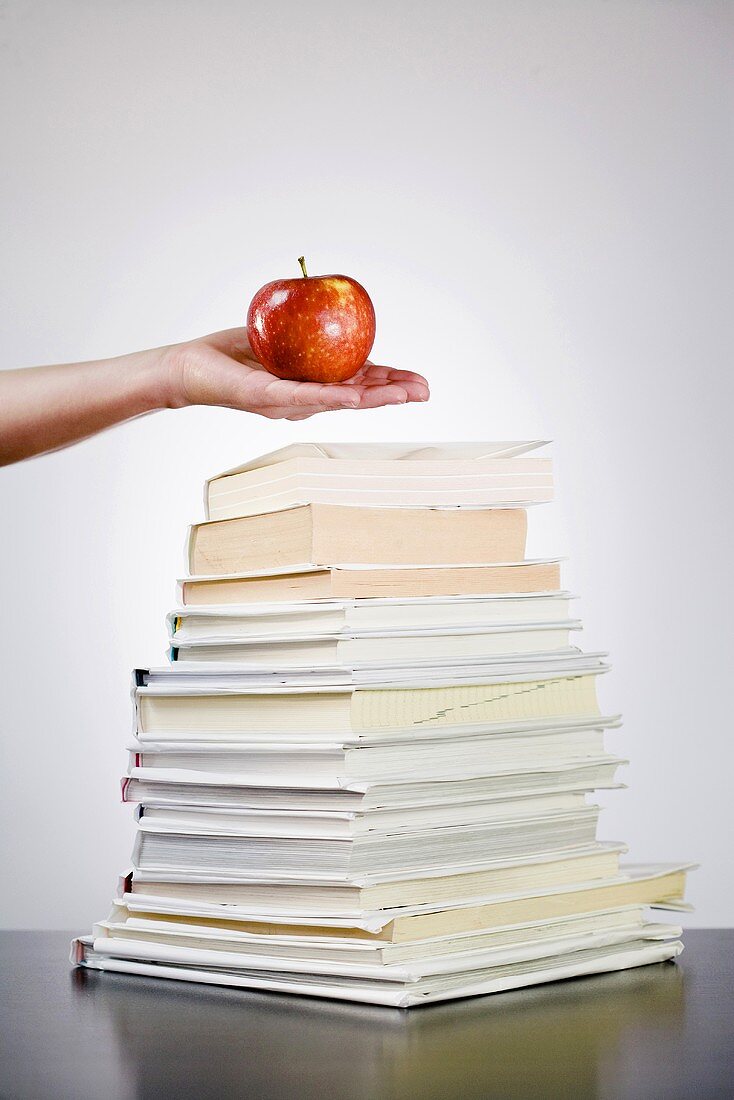 Hand holding an apple over a pile of books
