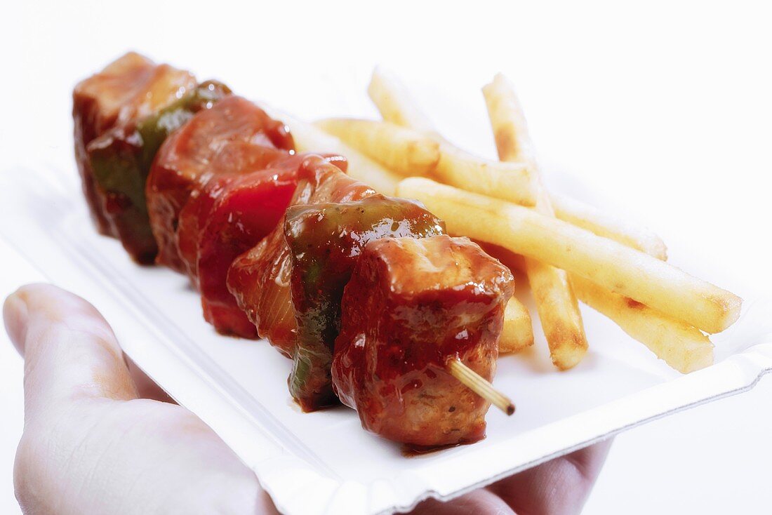 Man holding paper plate with shish kebab and french fries, close-up