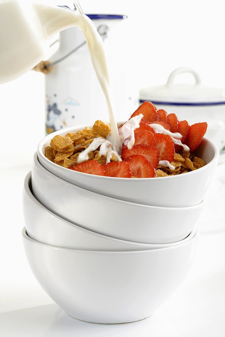 Pouring milk onto cornflakes and strawberries