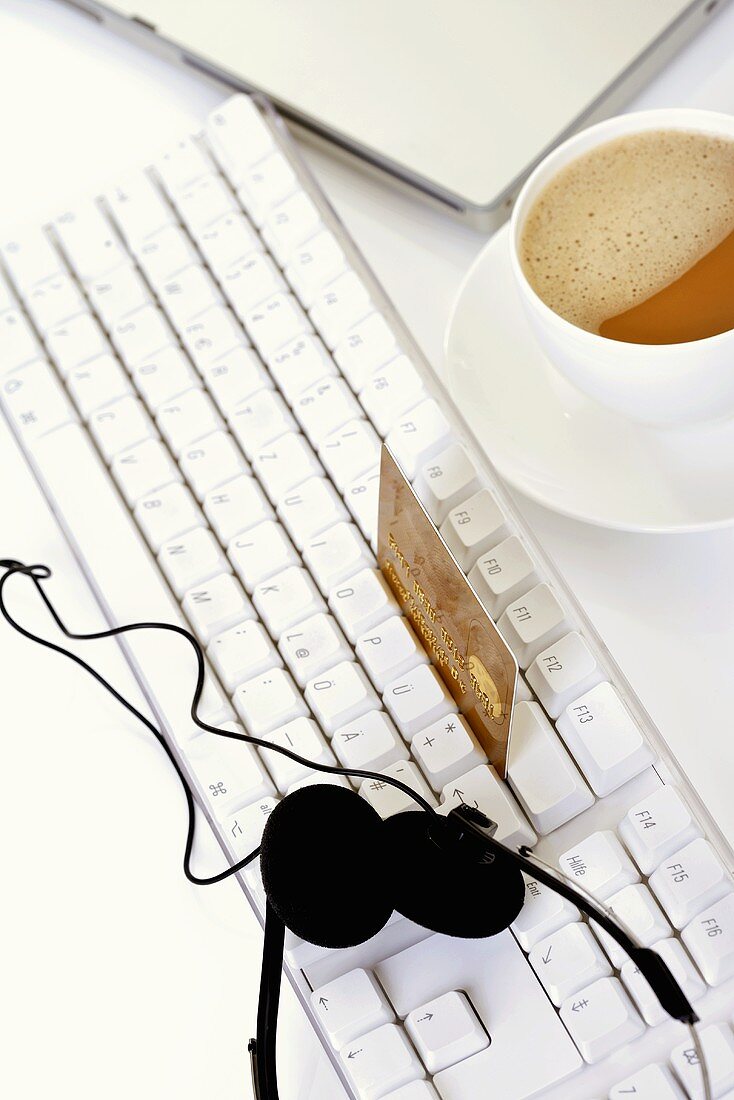 Kreditkarte auf Computertastatur, Kopfhörer, Kaffeetasse
