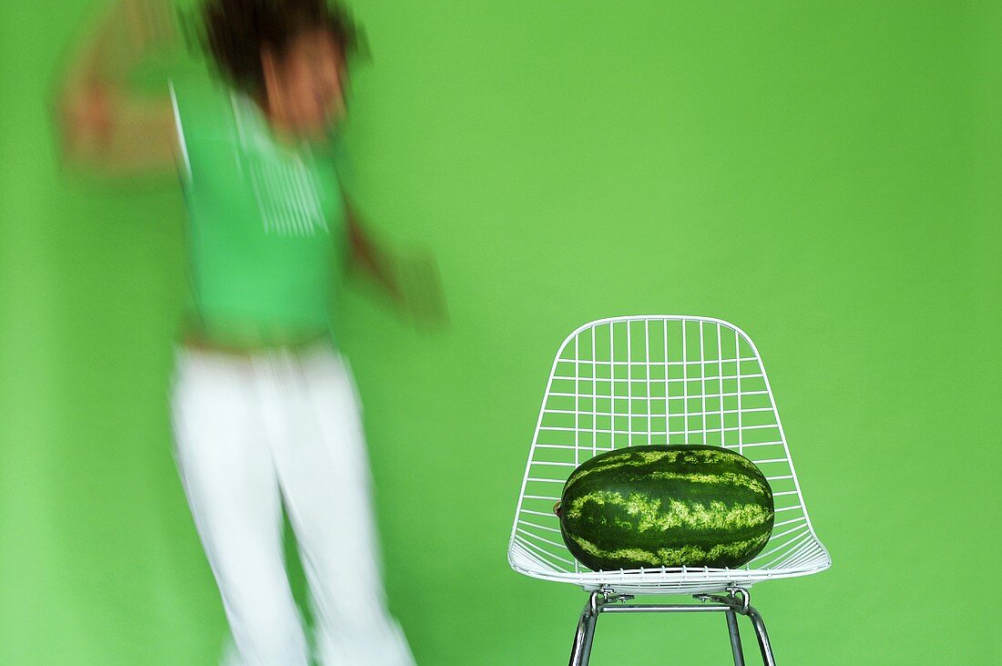 Wassermelone auf Stuhl, Frau macht Luftsprung