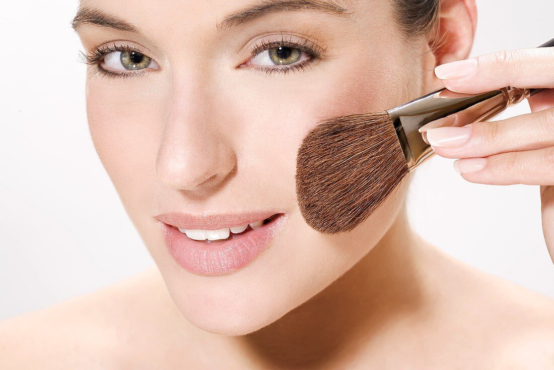 Young woman using make up brush, portrait