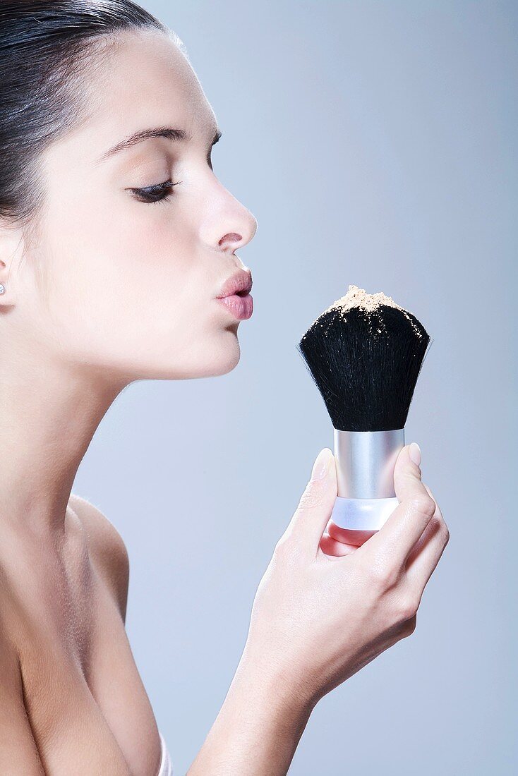 Young woman holding makeup brush, blowing, portrait