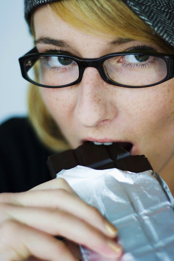 Junge Frau beisst in eine Tafel Schokolade